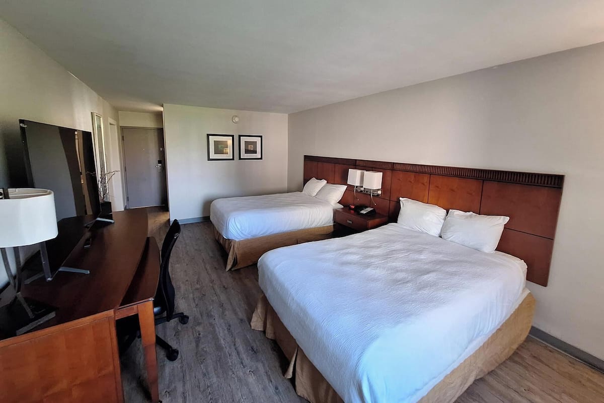 Ein Hotelzimmer mit zwei Betten, einem Schreibtisch, einem Stuhl, einem Fernseher und einem Spiegel.