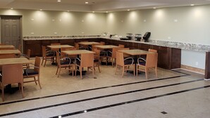 A spacious indoor area with multiple tables and chairs, a kitchen counter, and ventilation grilles on the ceiling. - The Hotel Orange (Orange)