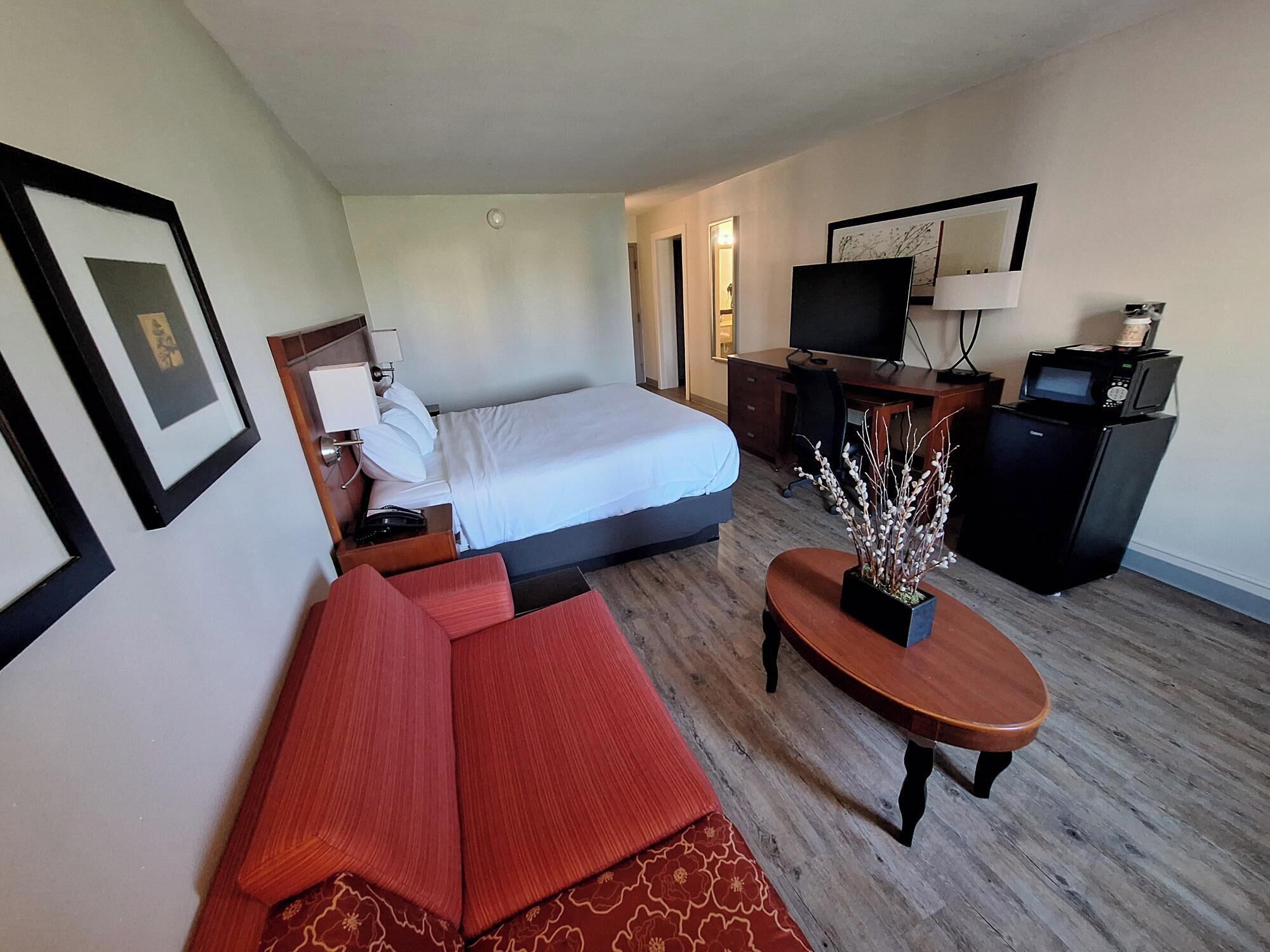 Habitación de hotel con cama, escritorio, televisor, cafetera y sofá.