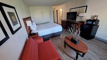 Habitación de hotel con cama, escritorio, televisor, cafetera y sofá.