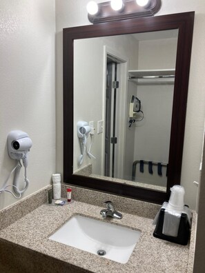 A bathroom with a sink, a mirror, a hairdryer, and a towel dispenser.
