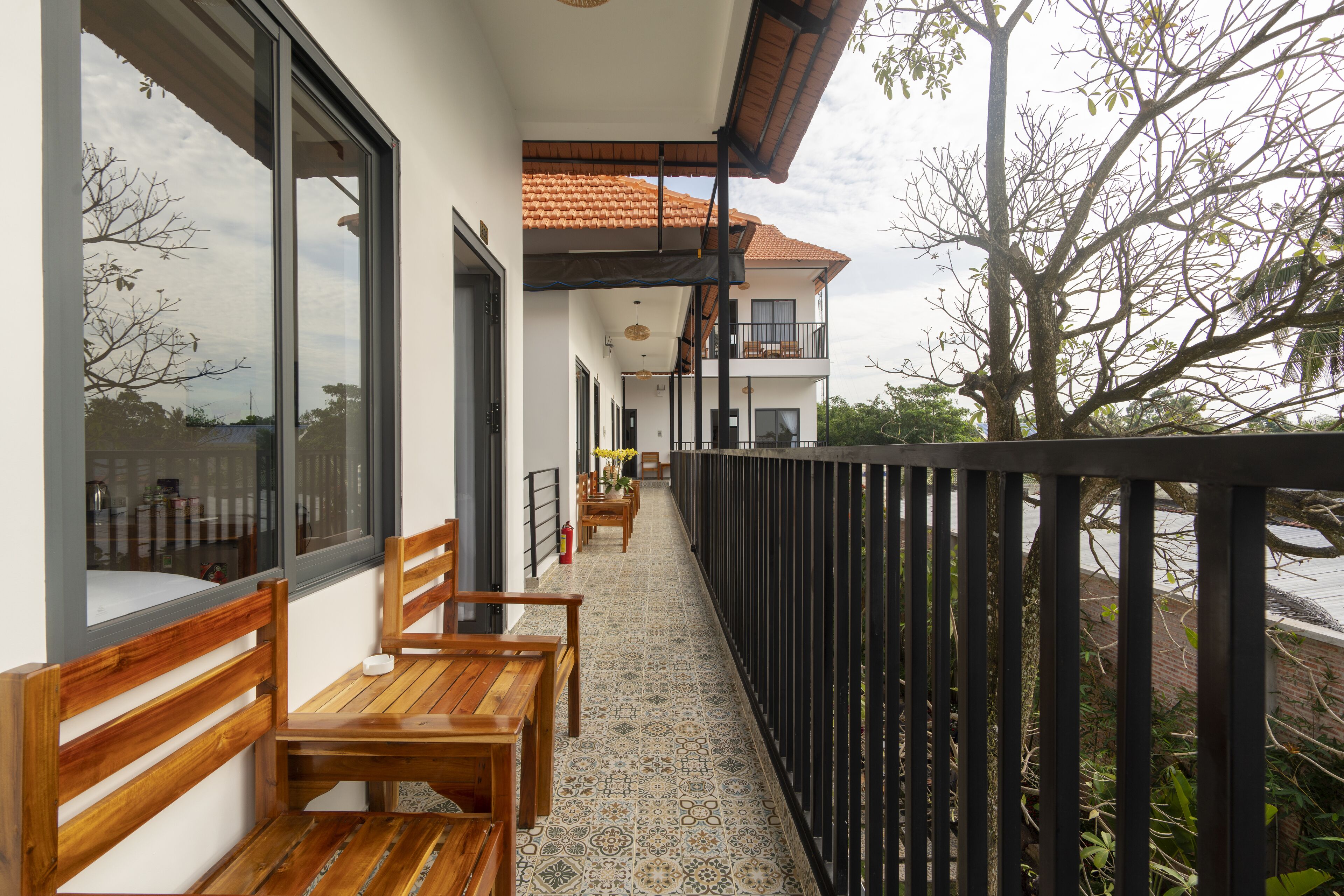 A balcony with wooden benches, a tiled floor, and a view of a tree and sky.