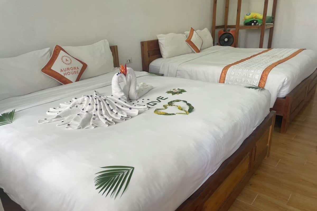 Deux lits doubles avec du linge de lit blanc, une tête de lit en bois et une petite étagère en bois sur laquelle sont posés un haut-parleur et des objets décoratifs.