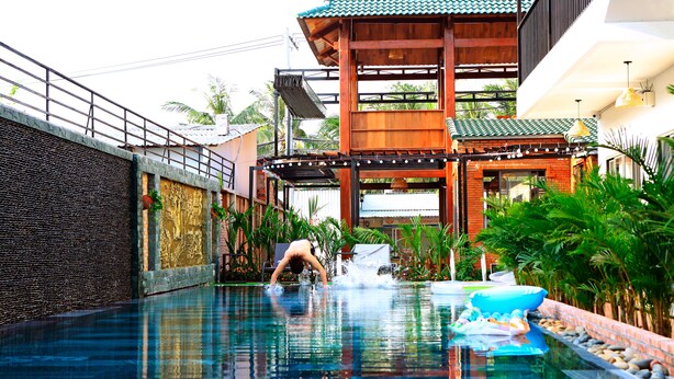 A swimming pool with a waterfall feature, surrounded by lush greenery and a traditional wooden structure. - Aurora House (Phu Quoc)