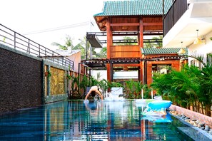 A swimming pool with a waterfall feature, surrounded by lush greenery and a traditional wooden structure. - Aurora House (Phu Quoc)