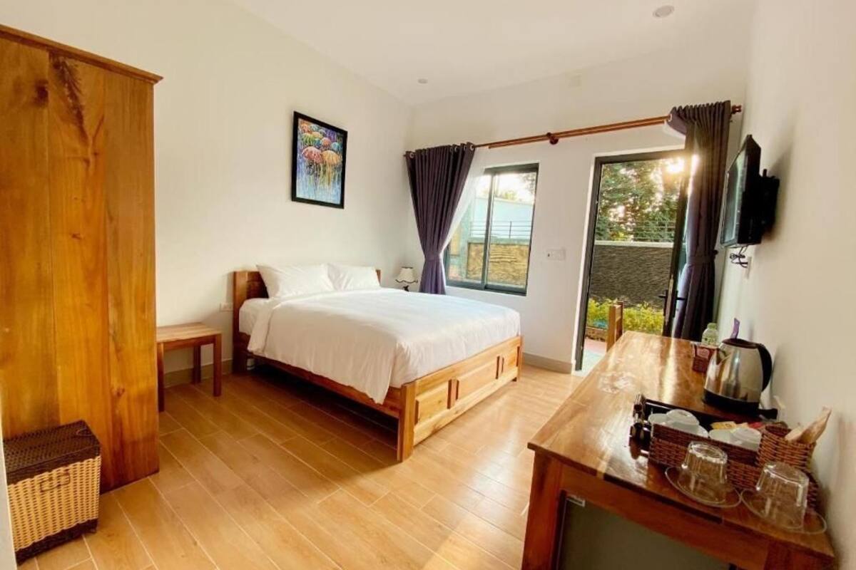 Une chambre à coucher avec un lit en bois, une petite table de chevet, une armoire en bois et un balcon avec des rideaux.