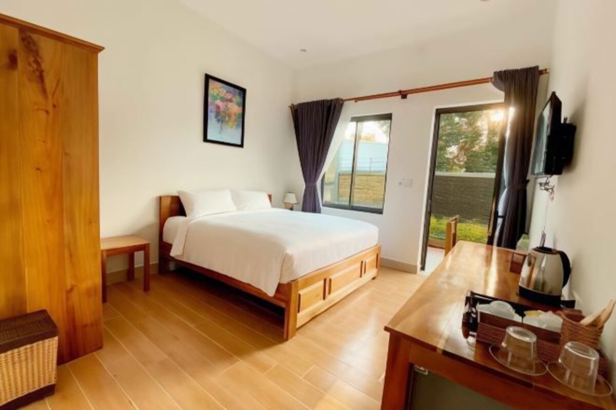 Un dormitorio con cama, un escritorio de madera con hervidor y vistas al exterior.