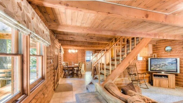 A log cabin interior with a dining area, staircase, and a television. - Enchanted Woods Cabin (Homewood)