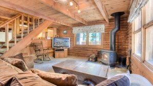 A cozy cabin interior with a wooden staircase, a television, a fireplace, and a rocking chair. - Enchanted Woods Cabin (Homewood)