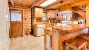 A log cabin interior with a kitchen, wooden cabinets, a stove, and a sink. - Enchanted Woods Cabin (Homewood)