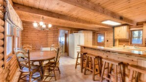 A wooden cabin interior with a dining table, chairs, a bar area, and a kitchen. - Enchanted Woods Cabin (Homewood)