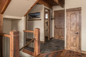 A wooden staircase with a metal railing leading to a room with a stone floor.