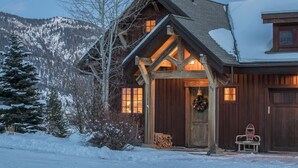 Ein rustikales Holzhaus mit einer Holzterrasse, einem Weihnachtskranz und einem schneebedeckten Berggrund.