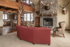 A spacious living room with a stone fireplace, a red sectional sofa, and a high wooden ceiling.
