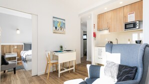 A modern living room with a sofa, a dining table with chairs, a kitchen area with cabinets and a microwave, and a painting on the wall. - Bright Valadim Apartment (Cascais)