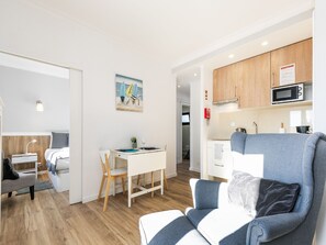 A modern living room with a sofa, a dining table with chairs, a kitchen area with cabinets and a microwave, and a painting on the wall. - Bright Valadim Apartment (Cascais)