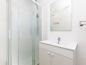 Une salle de bain moderne avec une douche à parois de verre, un lavabo blanc et un miroir au-dessus du meuble-lavabo.