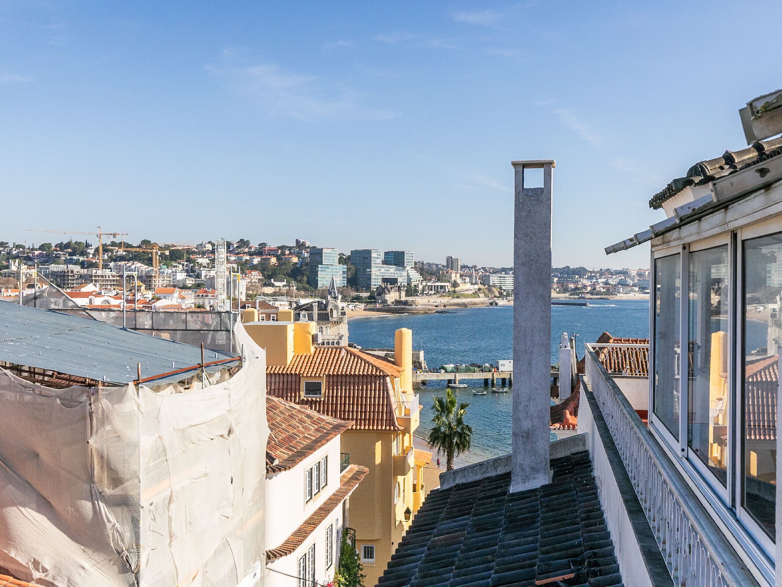 A coastal cityscape with a prominent tower, terraced buildings, and a clear view of the sea.