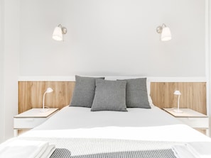 A modern bedroom with a large bed, two bedside tables with lamps, and a wooden headboard.