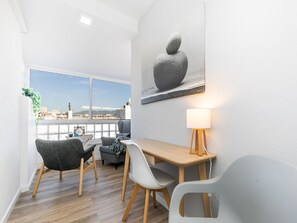 A modern room with a wooden desk, two chairs, a lamp, and a large window offering a city view.