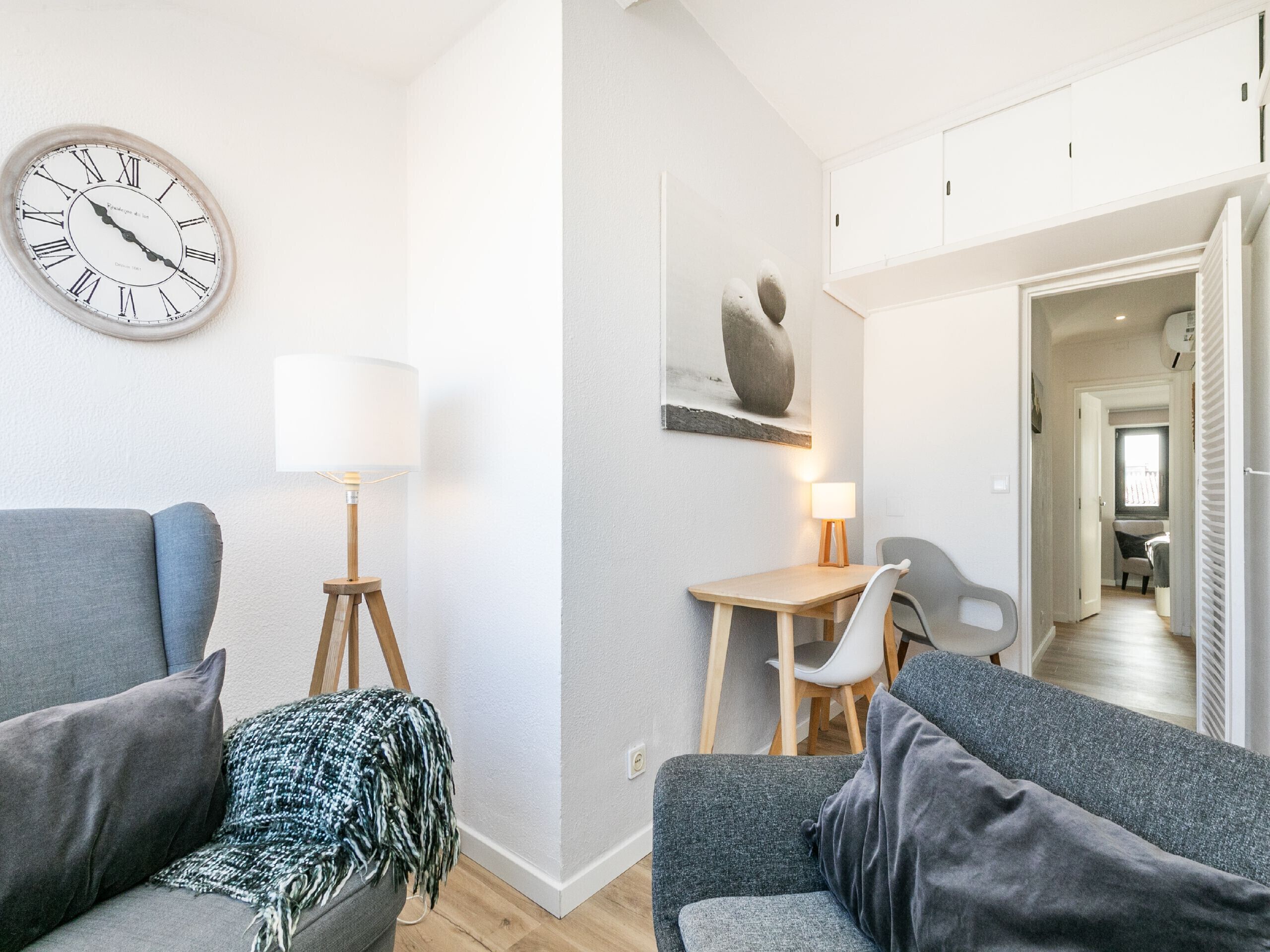 A modern living room with a sofa, a lamp, a dining table with chairs, and a wall clock.