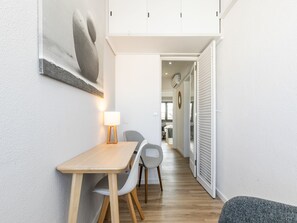 Un couloir étroit avec un coin repas comprenant une table et des chaises, une lampe fixée au mur et une porte donnant sur une autre pièce.