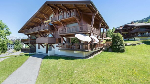 Una cabaña de madera de varios pisos, con balcones, una zona de estar al aire libre cubierta y una vista despejada del paisaje circundante.