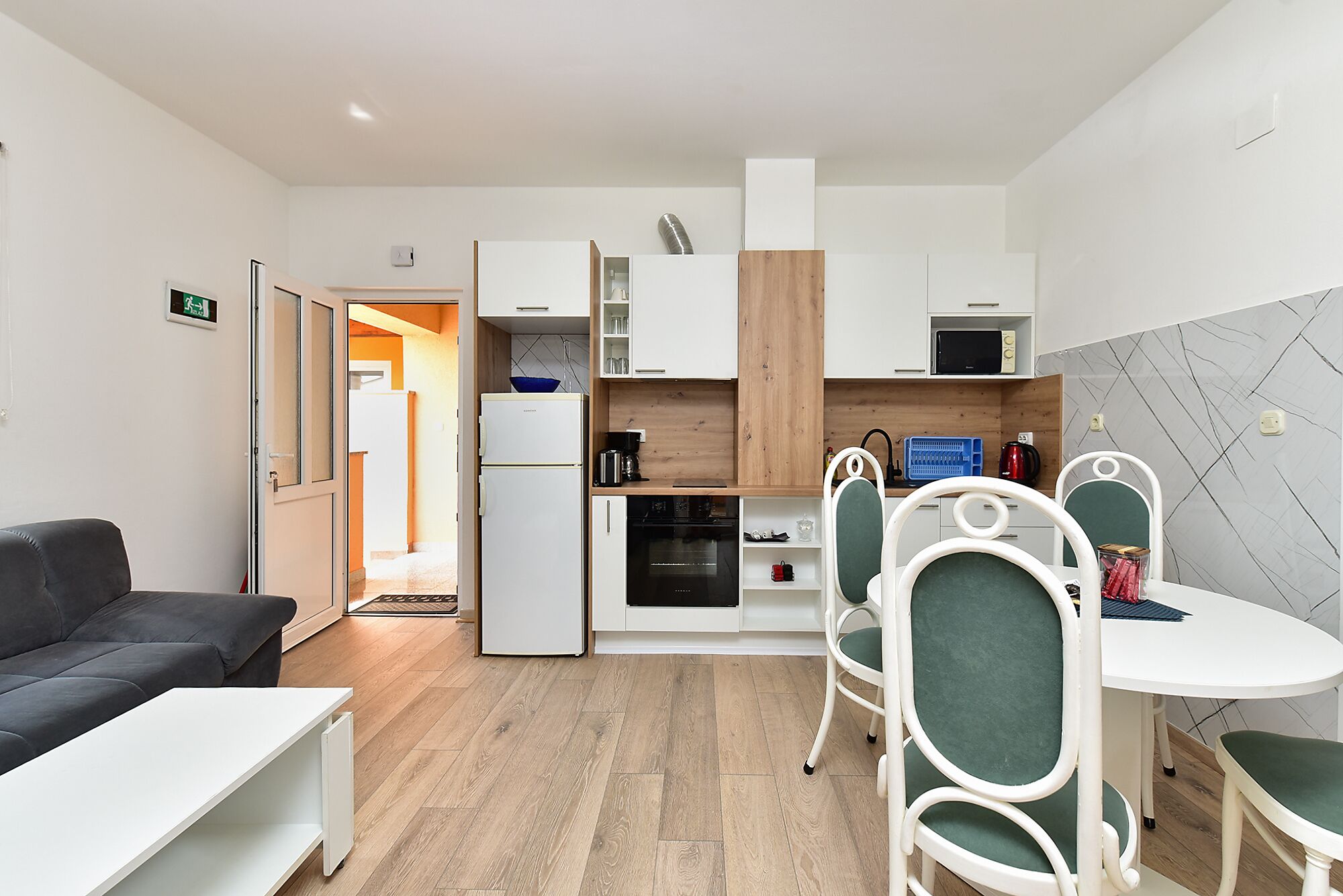 A compact hotel room with a kitchenette, a dining area with a table and chairs, and a sofa.