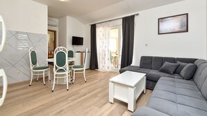 A living room with a grey sofa, a white coffee table, and a dining area with white chairs and a table. - Apartment 1985/27393 (Istria - Pula), 1000m from the beach (Pula)