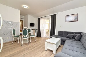 Una sala de estar con un sofá gris, una mesa de centro blanca y un comedor con sillas y una mesa blancos.