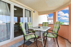 Ein Balkon mit Tisch und vier Stühlen, eine Schiebeglastür und Blick auf ein Gebäude mit Ziegeldach.