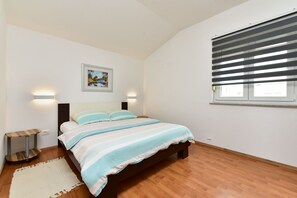 A bedroom with a bed, a painting on the wall, a window with blinds, and a wooden floor.