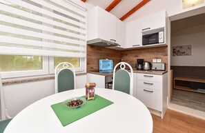 A compact kitchen with a microwave, coffee maker, and toaster on the counter, a dining table with chairs, and a window with blinds.