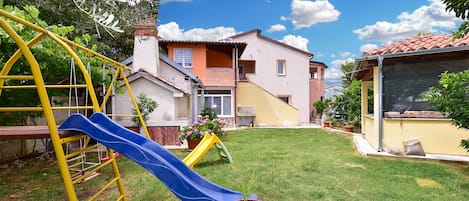 A residential area with a playground featuring a slide, a yellow swing set, and a green climbing frame.