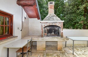 Une cheminée extérieure en briques avec un conduit de cheminée en pierre, une table et une chaise, le tout installé dans un espace patio.