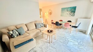 A living room with a beige sofa, a coffee table, and a dining area with a table and chairs. - Branly 2,2 bedrooms and 1 parking (Cannes)