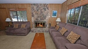 A cozy living room with a stone fireplace, two sofas, a coffee table, and large windows.