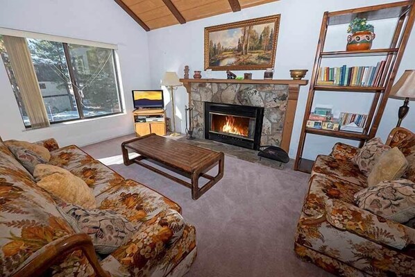 A living room with a fireplace, floral-patterned sofas, a coffee table, a bookshelf, and a television. - Economical Ski Home with Community Hot Tub and Seasonal Pool Acess! (South Lake Tahoe)