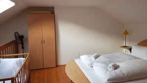 Een slaapkamer met een houten bed, een houten garderobe, een klein tafeltje met een lamp en een ventilator.