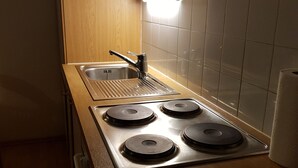 Een kleine keuken met een roestvrijstalen spoelbak, een vierpits fornuis, houten kastjes en witte betegelde muren.