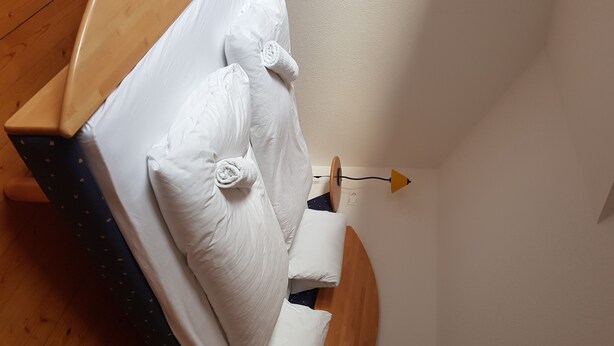 Een bed met witte lakens en kussens, een houten hoofdbord en een nachtkastje met een lamp.