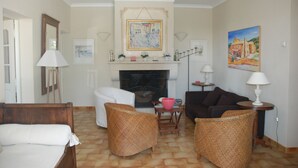 A living room with a fireplace, wicker furniture, and artwork on the walls. - Provence ideally located in the middle of vineyards, single storey villa 8 pers. (Gigondas)