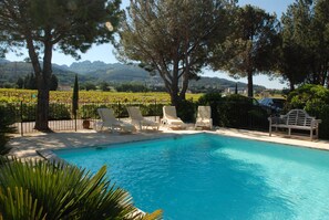 A pool with lounge chairs and a bench, surrounded by trees and a vineyard in the background. - Provence ideally located in the middle of vineyards, single storey villa 8 pers. (Gigondas)
