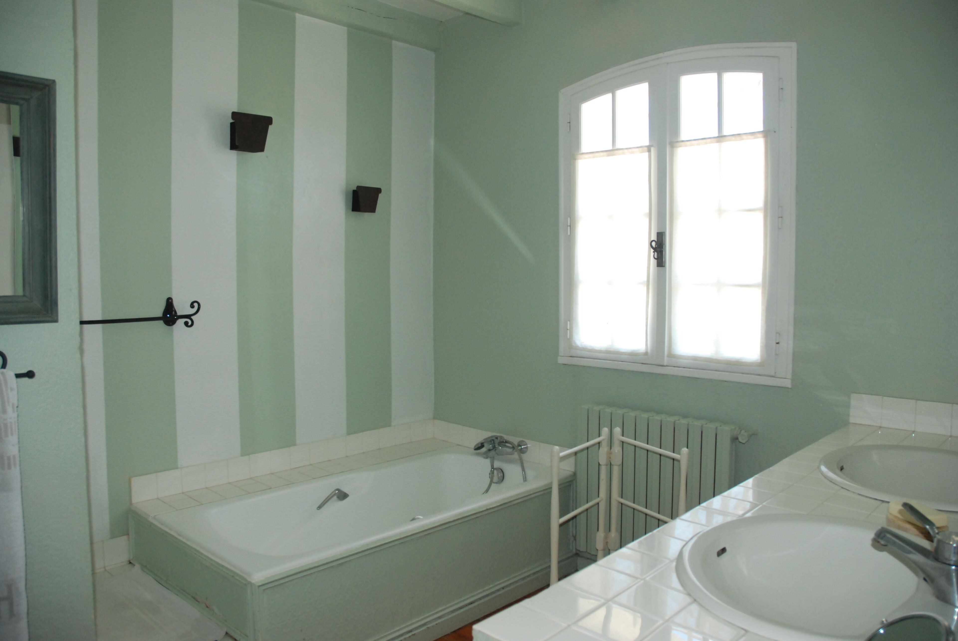 Une salle de bain avec une baignoire, deux lavabos, une fenêtre et un radiateur.