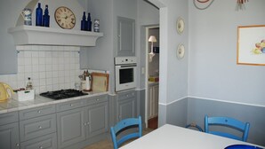 A kitchen with grey cabinets, a white countertop, a stove, and a microwave. There are blue chairs at a table, and a chandelier hangs from the ceiling. - Provence ideally located in the middle of vineyards, single storey villa 8 pers. (Gigondas)