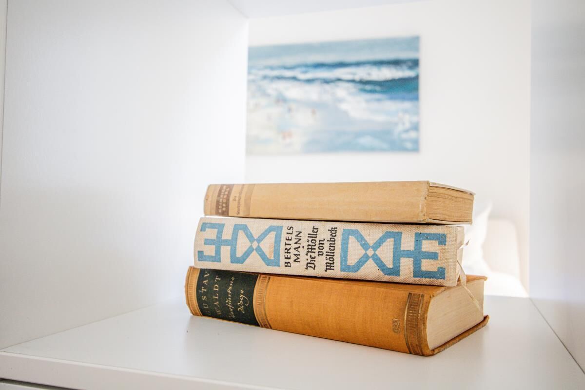 A stack of books on a white surface with a painting of a beach in the background.