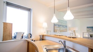 A modern kitchen with a stainless steel sink, wooden countertop, and pendant lights. - Small hideaway<br>- A very special domicile in the middle of Friedrichstrasse -<br>The large double bed (180x200, mattress size approx. 1.92 m x 90 cm) is located in the modern living room, separated by a room divider. The flat screen TV. (Westerland)