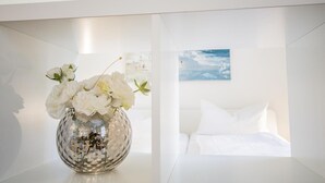 A white room with a bed and a wall-mounted painting. - Small hideaway<br>- A very special domicile in the middle of Friedrichstrasse -<br>The large double bed (180x200, mattress size approx. 1.92 m x 90 cm) is located in the modern living room, separated by a room divider. The flat screen TV. (Westerland)