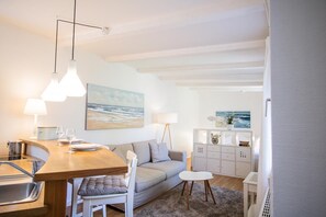 A modern kitchen with a wooden countertop, white cabinets, and a dining area with a grey sofa and a small round table. - Small hideaway<br>- A very special domicile in the middle of Friedrichstrasse -<br>The large double bed (180x200, mattress size approx. 1.92 m x 90 cm) is located in the modern living room, separated by a room divider. The flat screen TV. (Westerland)