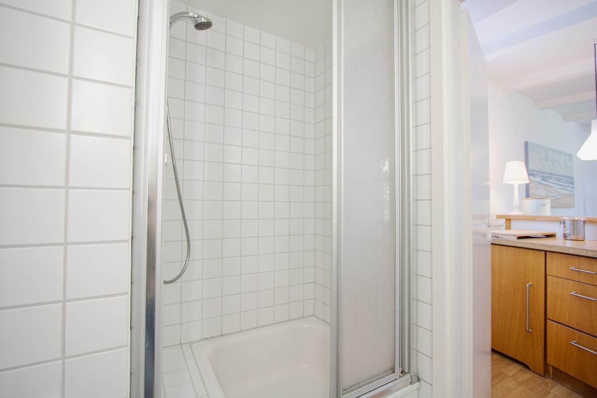 A modern bathroom with white tiled walls, a glass shower enclosure, and wooden cabinets.